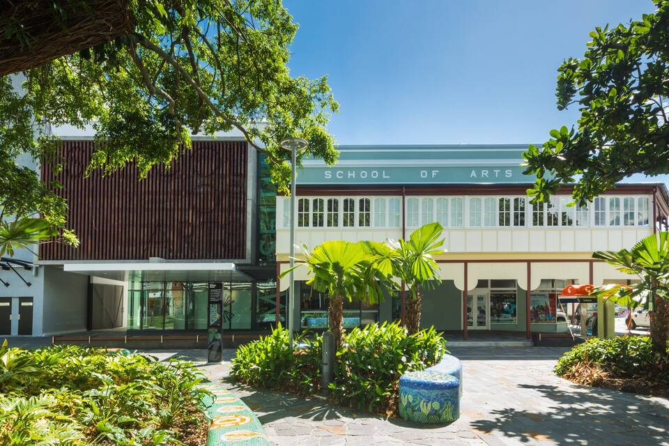 A School of Arts building with a modern facade, surrounded by lush greenery and a paved courtyard.