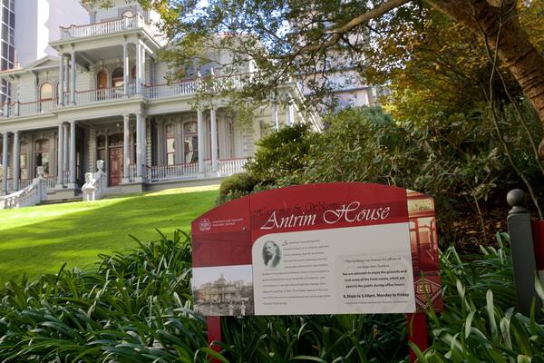 A historic house with a large porch and a sign in the foreground.