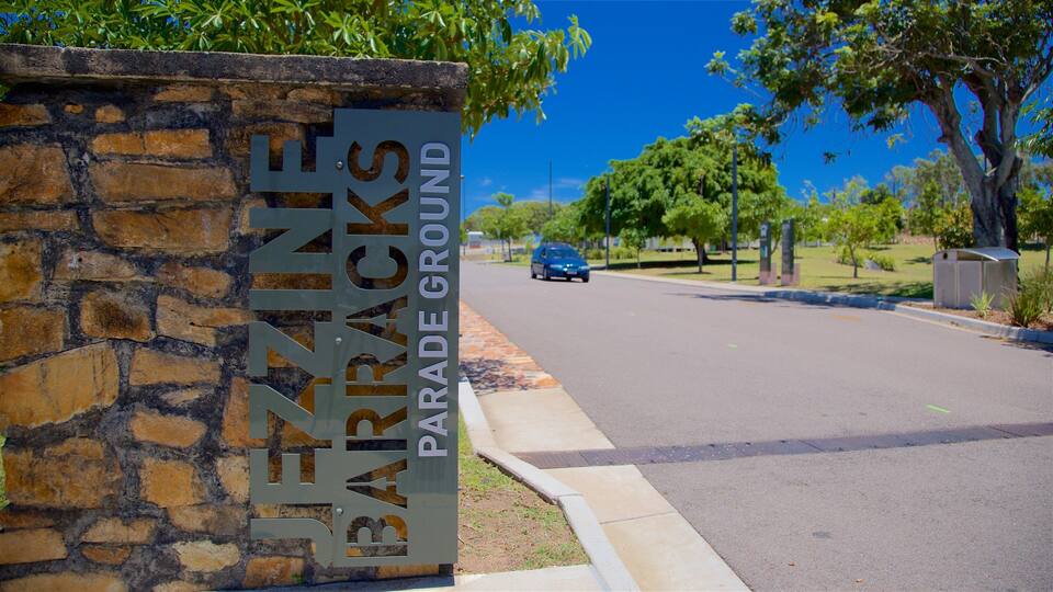 A street sign for 'JEZINE PARADE GROUND' with a stone wall and trees in the background.