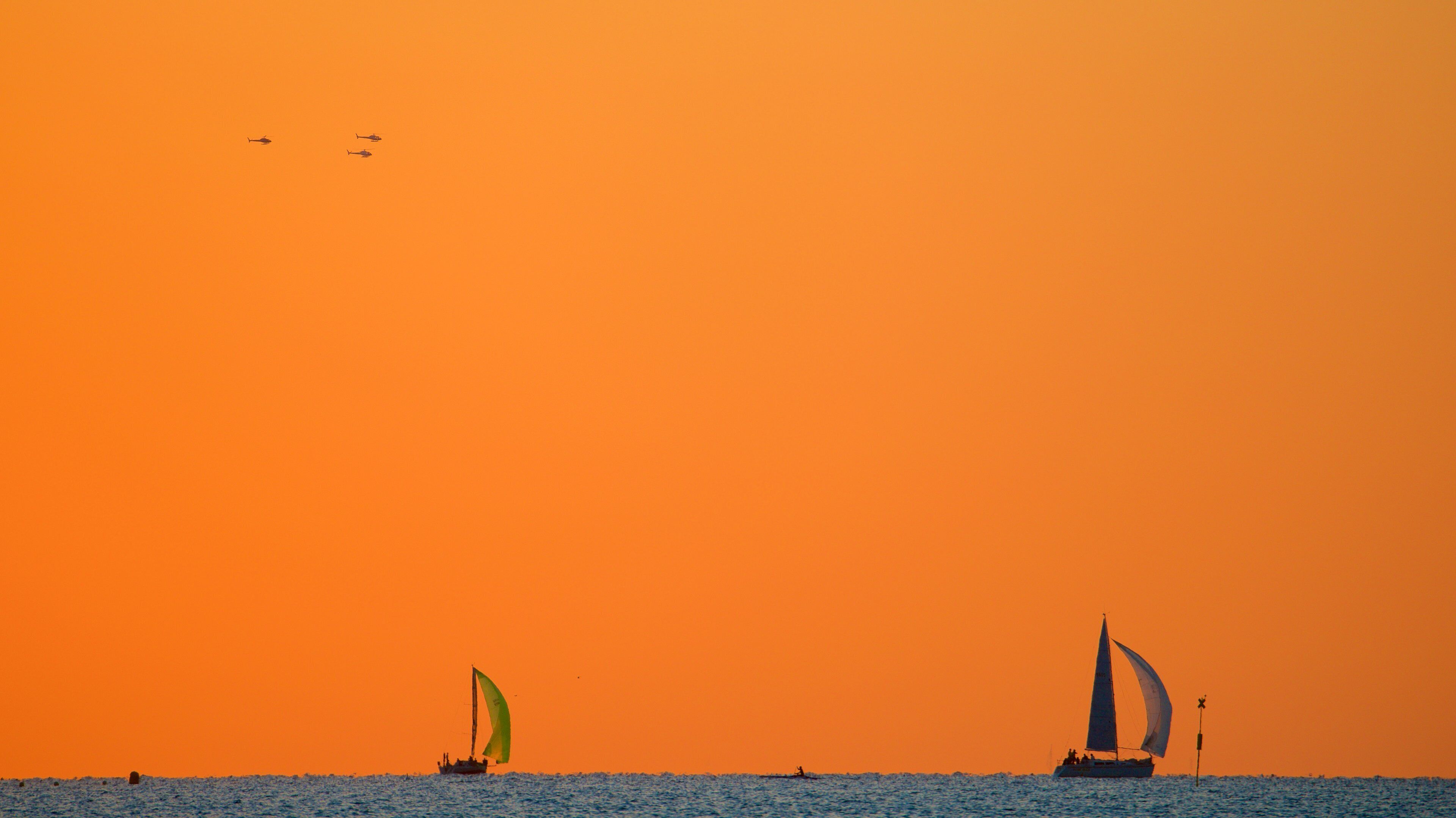 A sunset over the ocean with two sailboats and a small boat in the distance.