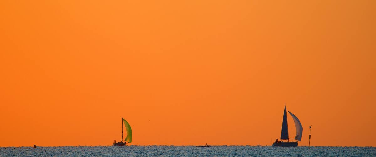 A sunset over the ocean with two sailboats and a small boat in the distance.