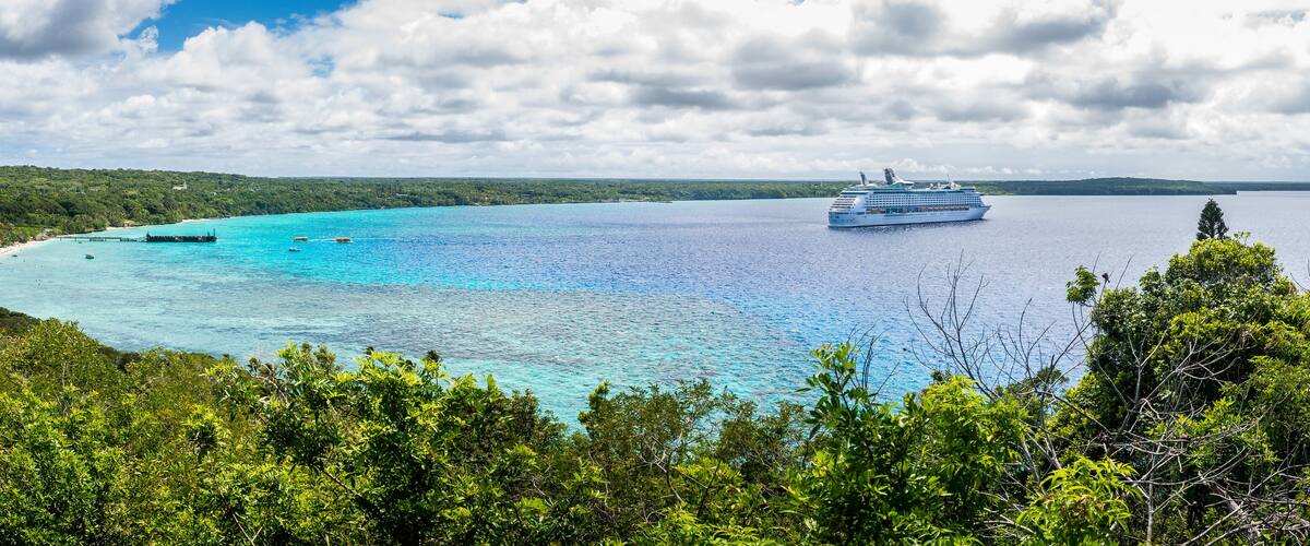 A cruise ship on a turquoise sea with a forested coastline.