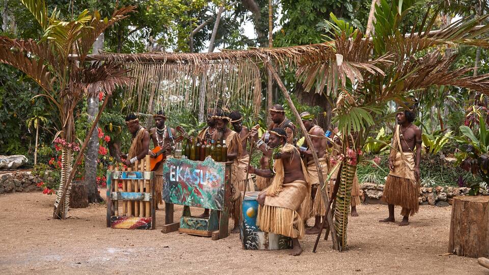A group of people in traditional attire performing music outdoors with a sign that reads "EKASIA".