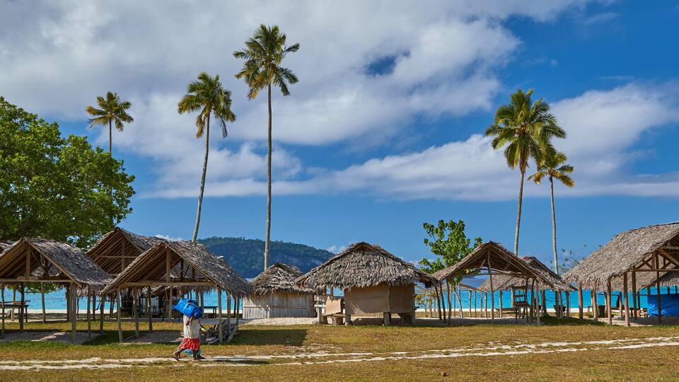 A beach with thatched-roof huts and palm trees under a clear sky.