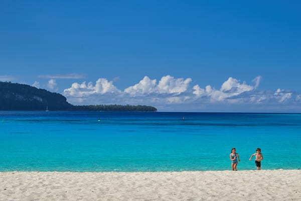 Une plage à l’eau turquoise et limpide, un rivage sablonneux et, au loin, une île avec une colline couverte de végétation.
