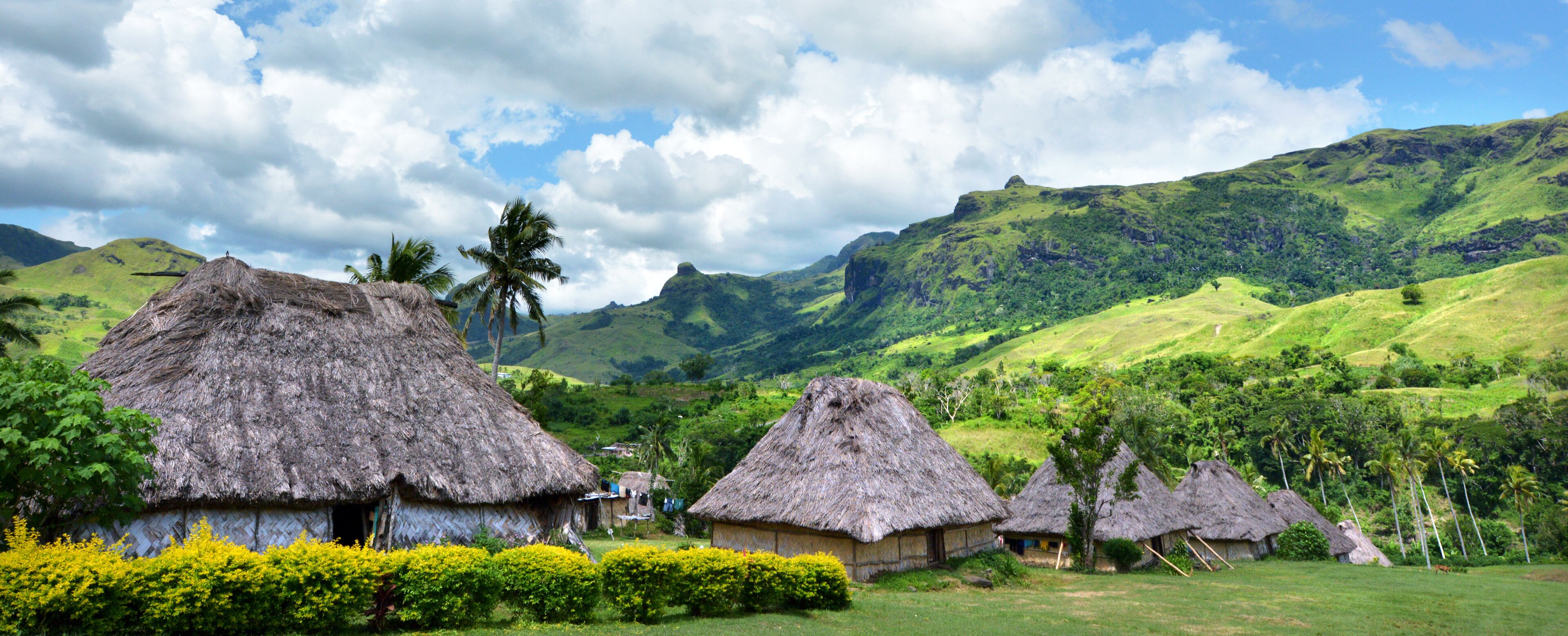 Thatched-roof huts in a lush green valley with mountains in the background.
