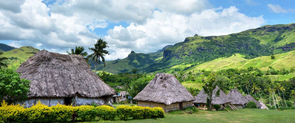 Thatched-roof huts in a lush green valley with mountains in the background.