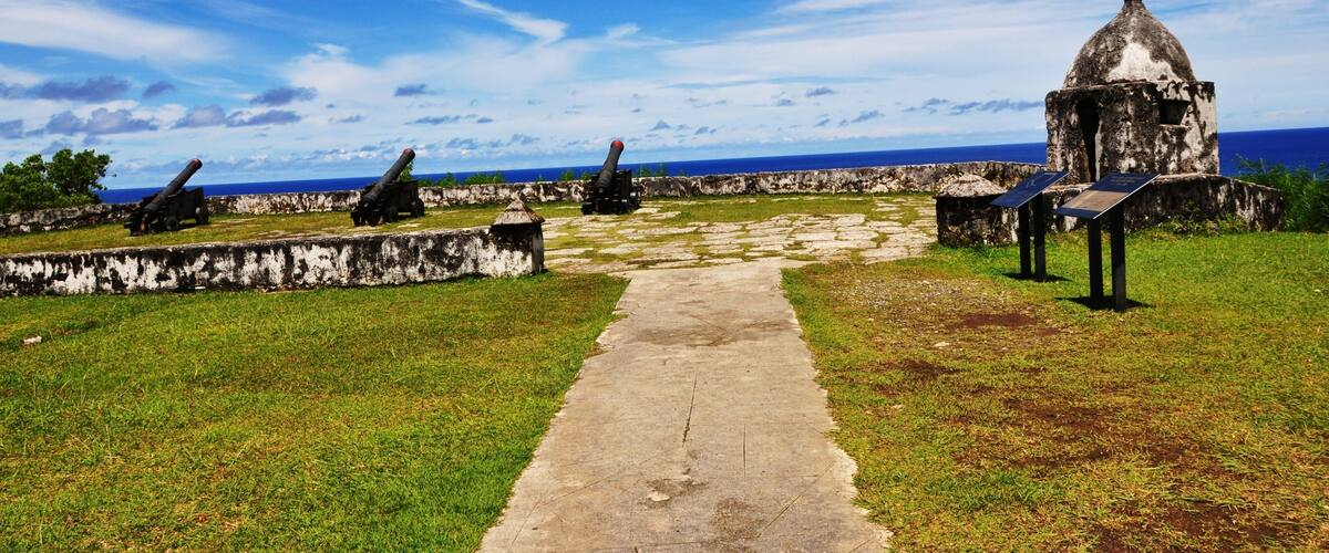 A coastal fort with cannons, a clear sky, and a pathway leading to a small building.