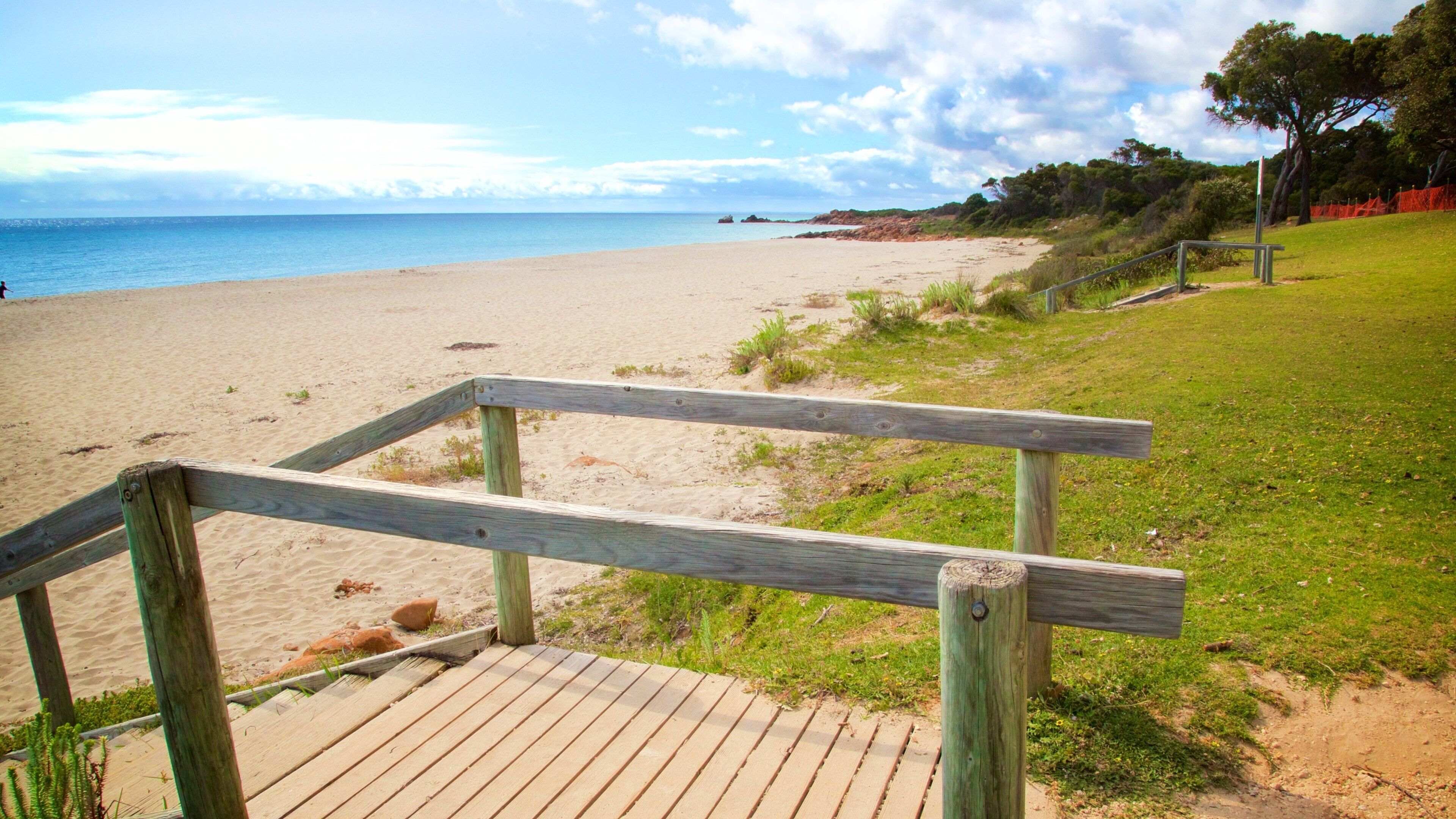 A wooden boardwalk leading to a sandy beach with a clear sky and distant mountains.