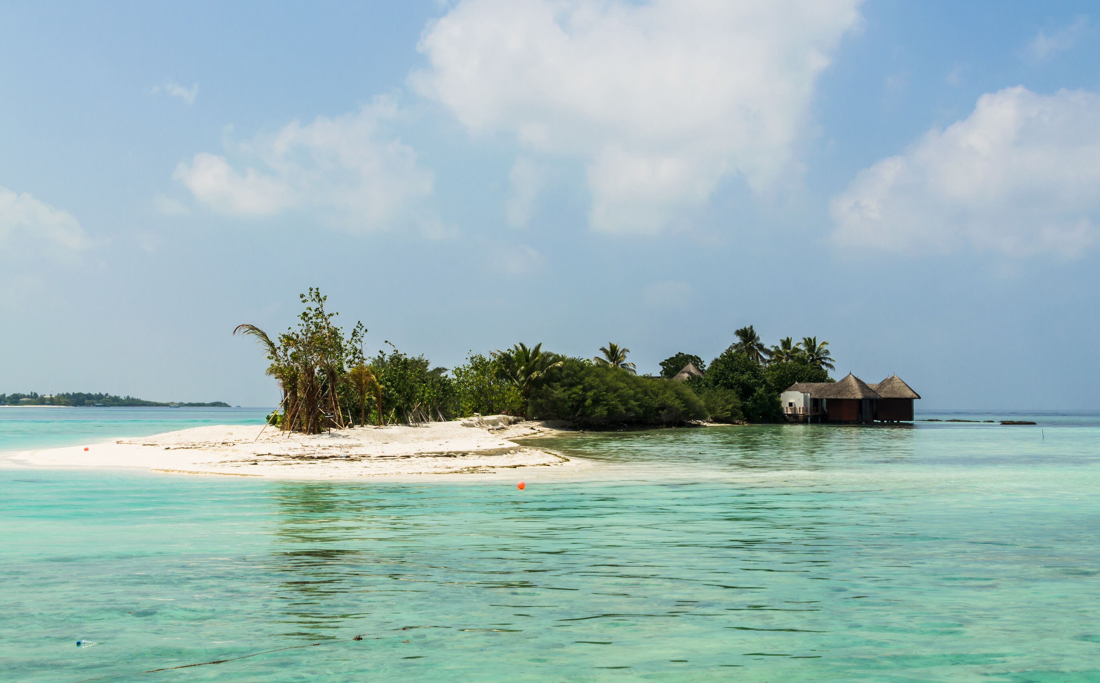 Вeautiful wooden villas, standing on stilts on tiny island in the middle of turquoise, transparent water of the Indian Ocean, against the blue sky and green palm trees, Maldives. Travel and tourism co