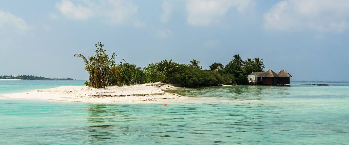 Вeautiful wooden villas, standing on stilts on tiny island in the middle of turquoise, transparent water of the Indian Ocean, against the blue sky and green palm trees, Maldives. Travel and tourism co