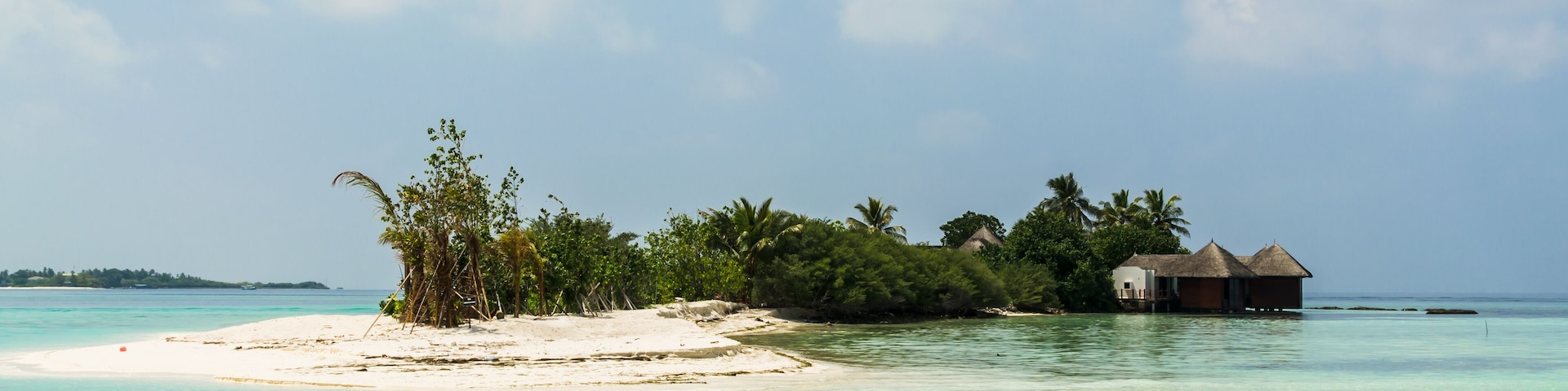 Вeautiful wooden villas, standing on stilts on tiny island in the middle of turquoise, transparent water of the Indian Ocean, against the blue sky and green palm trees, Maldives. Travel and tourism co
