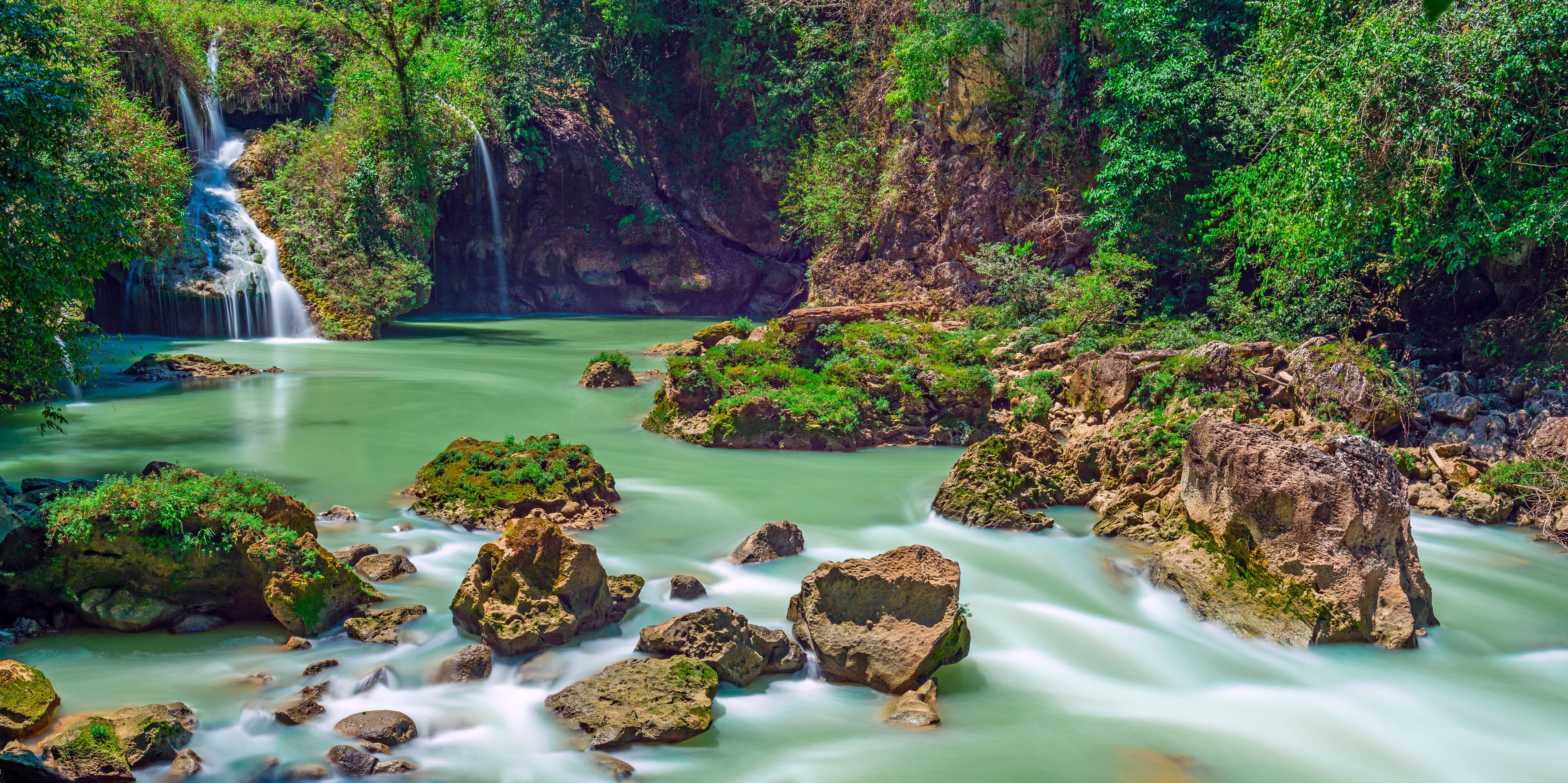 A waterfall, a river, and rocky terrain with greenery.