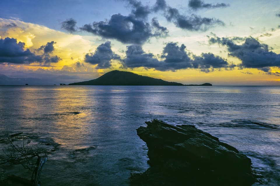 Ein Sonnenuntergang über einem ruhigen Meer mit einer felsigen Küstenlinie und einer entfernten Insel.