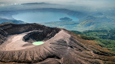 Un cratère volcanique abritant un lac, entouré de montagnes et de zones boisées.