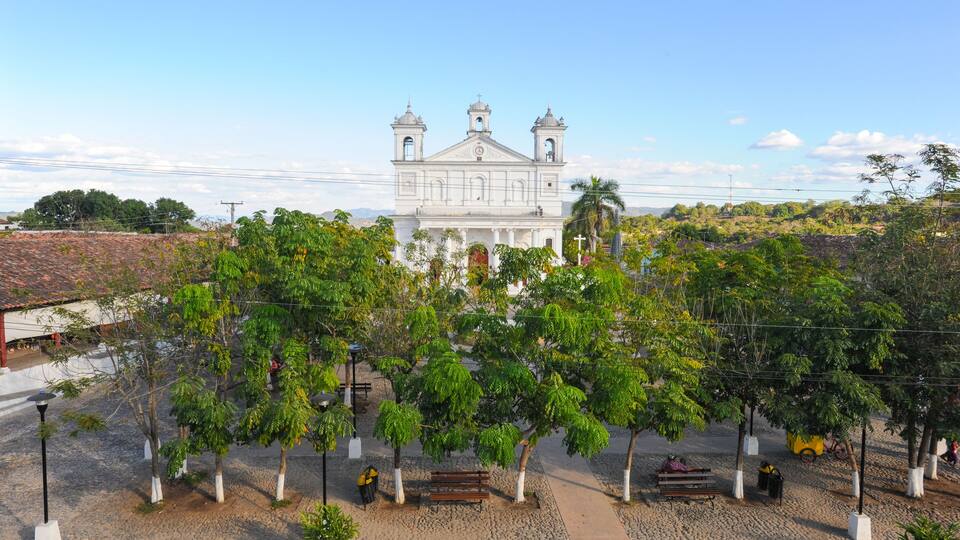 A white church with two towers, surrounded by trees and a paved area with benches.