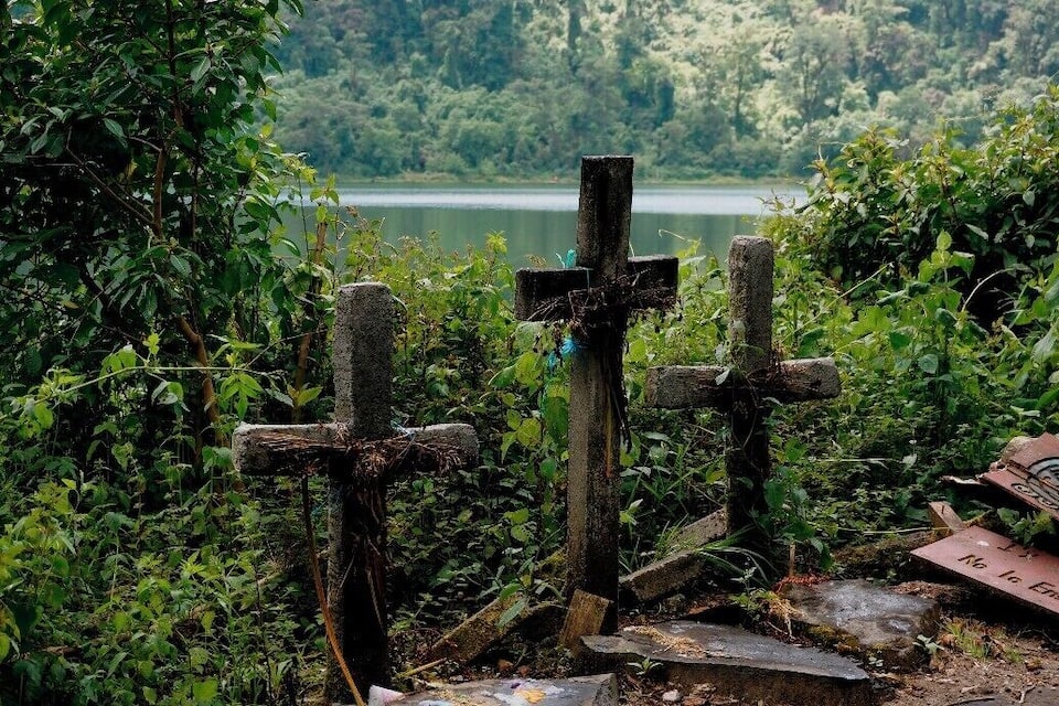 Uma cruz em uma área verde e exuberante, com um lago ao fundo.