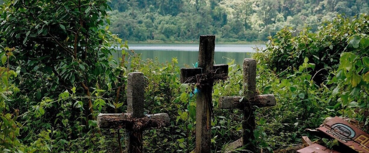 A cross in a lush, green area with a lake in the background.