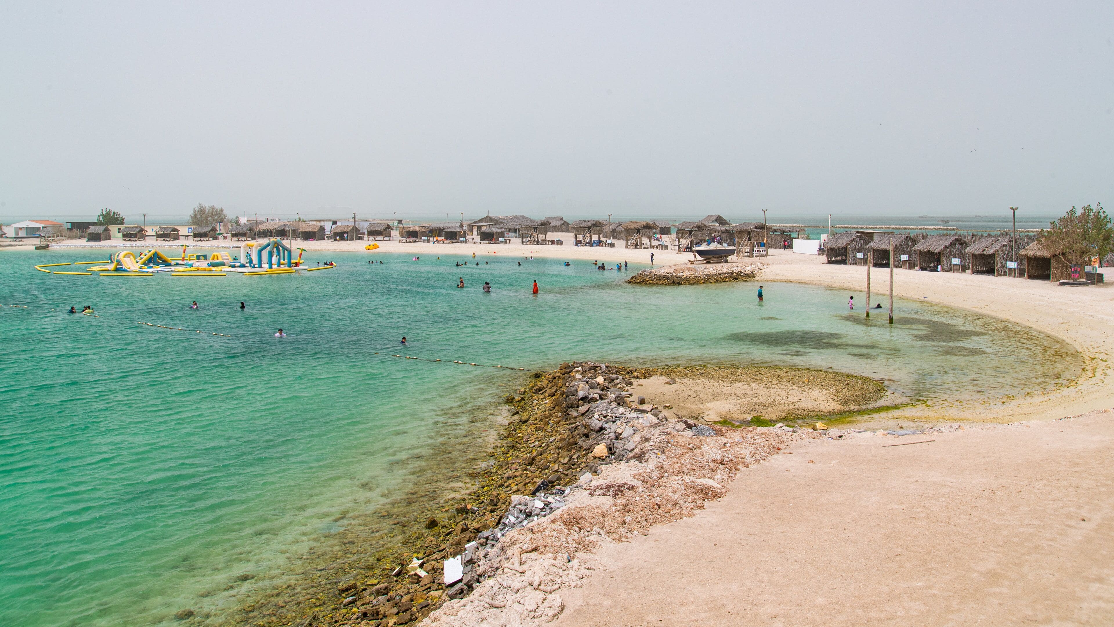 A beach with clear turquoise water, a sandy shore, and thatched-roof huts.