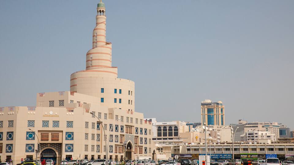 A large mosque with a tall minaret, surrounded by modern buildings and a busy street.