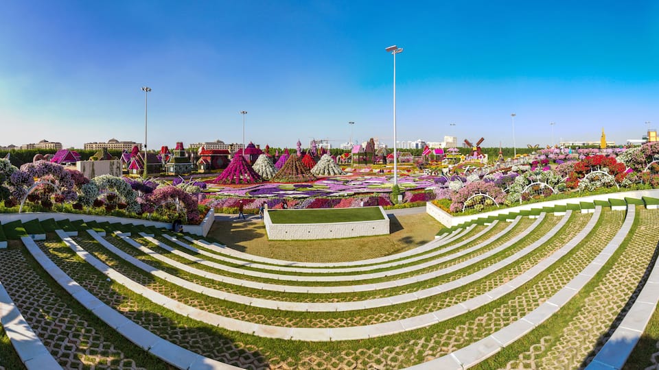 Jardim ajardinado com canteiros escalonados de flores e um gramado central.
