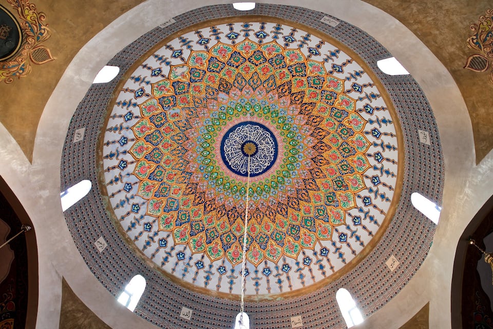 Um mosaico circular detalhado com padrões intrincados e caligrafia árabe em um teto abobadado.