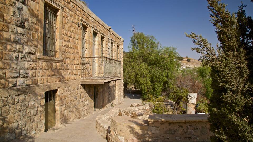 A stone building with a balcony, surrounded by trees and a clear sky.