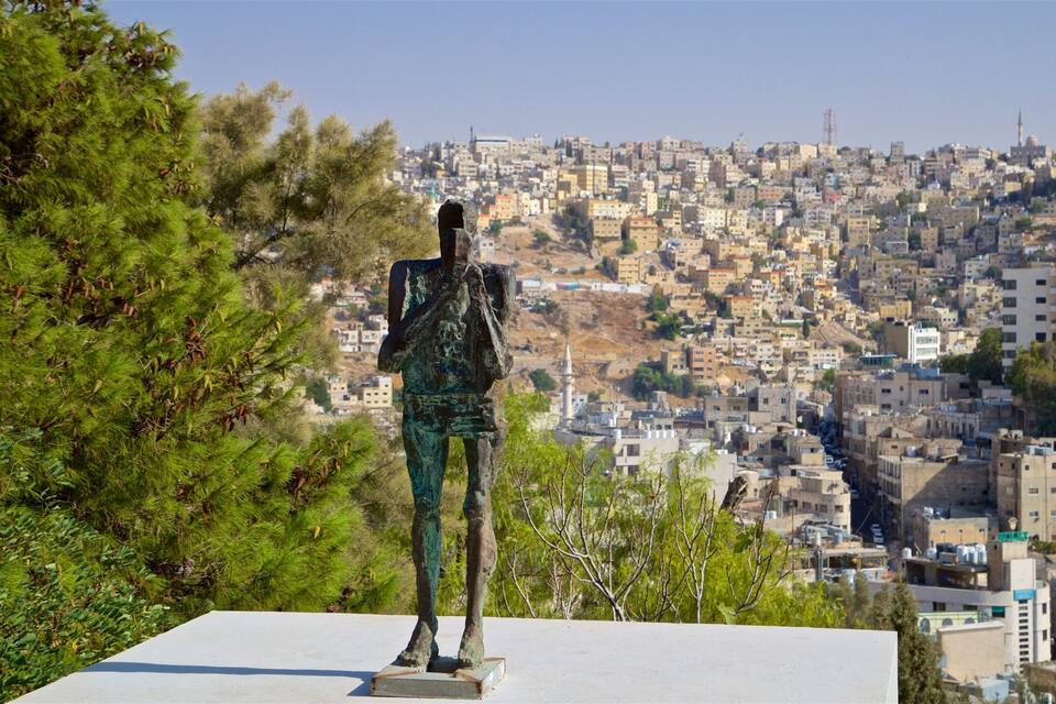 Uma estátua em um pedestal com vista para uma cidade densamente povoada, com uma mesquita em destaque ao fundo.