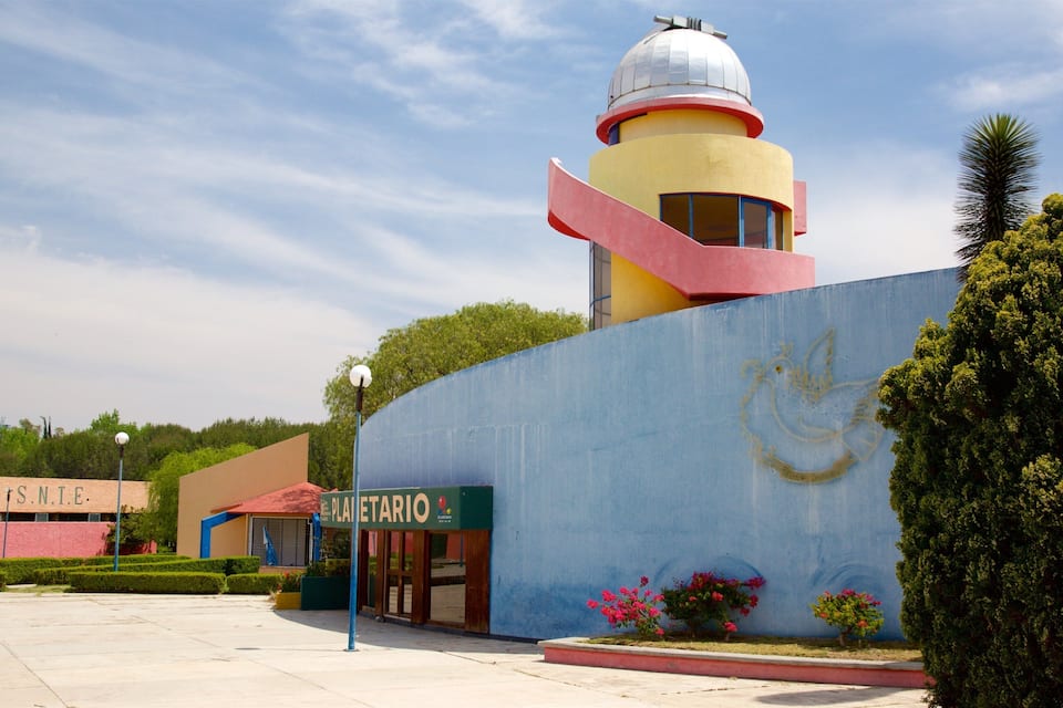 Um edifício colorido com uma cúpula, uma placa com o texto "PLATELARIO" e um mural de um pássaro em uma parede.