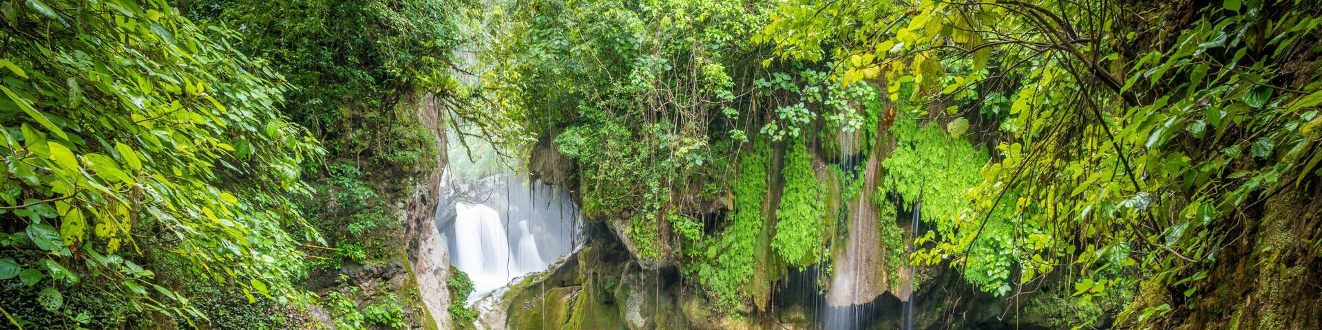 A waterfall cascading into a clear blue pool surrounded by lush greenery and rocky terrain.