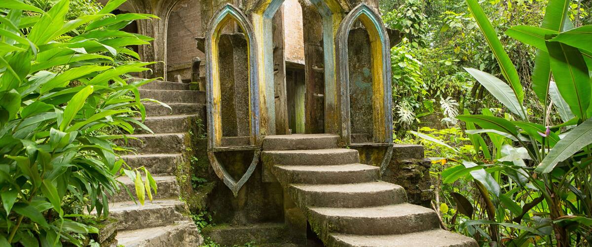 A stone staircase leading up to a gothic archway surrounded by lush greenery.
