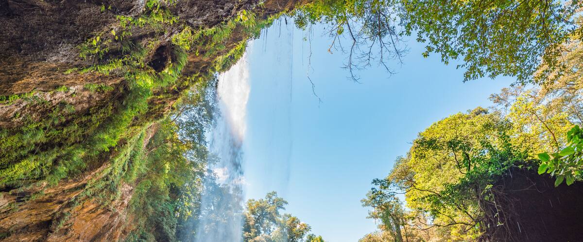 A waterfall cascading into a river surrounded by lush greenery and rocky cliffs.