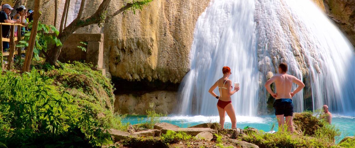 A waterfall cascading into a turquoise pool surrounded by lush greenery and rocky cliffs.