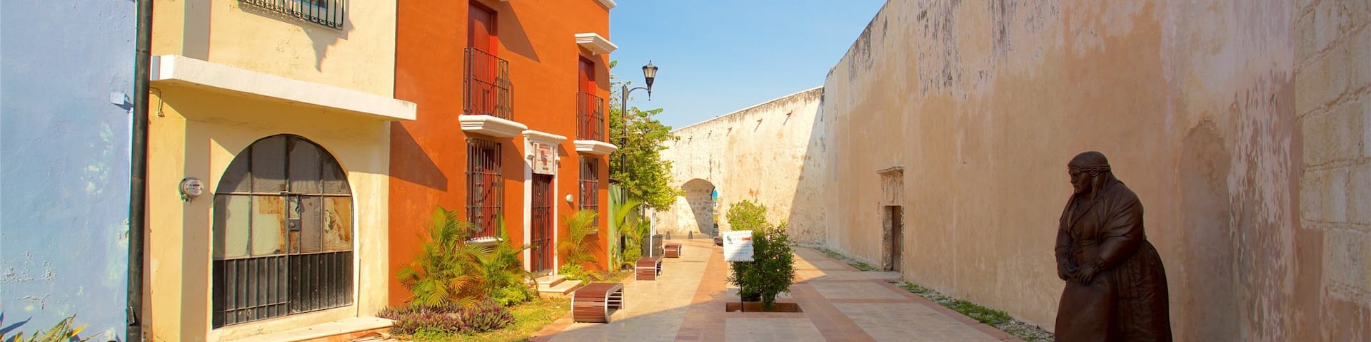 A narrow street with buildings painted in orange and white, a statue, and a clear blue sky.