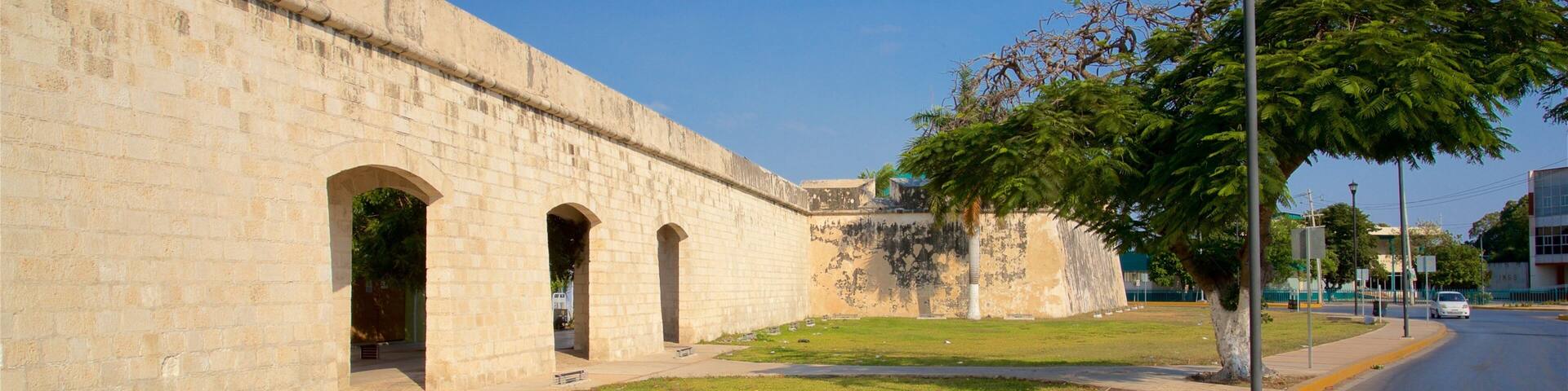 A historic stone wall with arches, a sidewalk, and a street with a car.