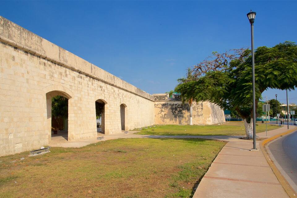 Un mur de pierre ancien, doté d’arcades, un trottoir et une rue où se trouve une voiture.