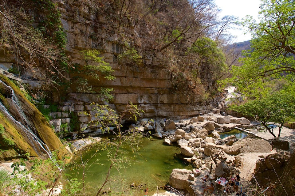 A waterfall cascading down a rocky cliff into a small pond surrounded by boulders and trees.