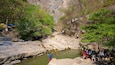 A rocky riverbed with water, surrounded by trees and a cliff.