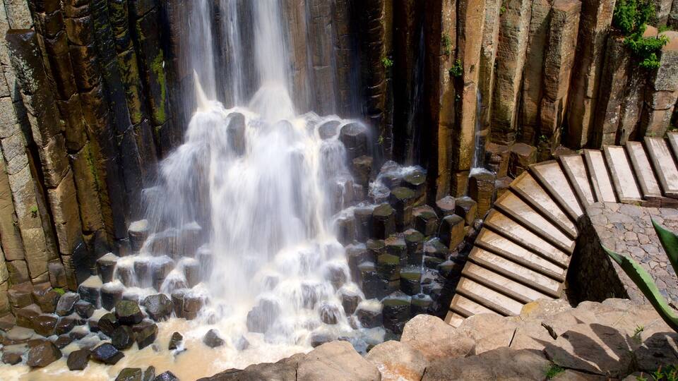 A waterfall cascading over rocks into a pool, surrounded by stone steps and greenery.