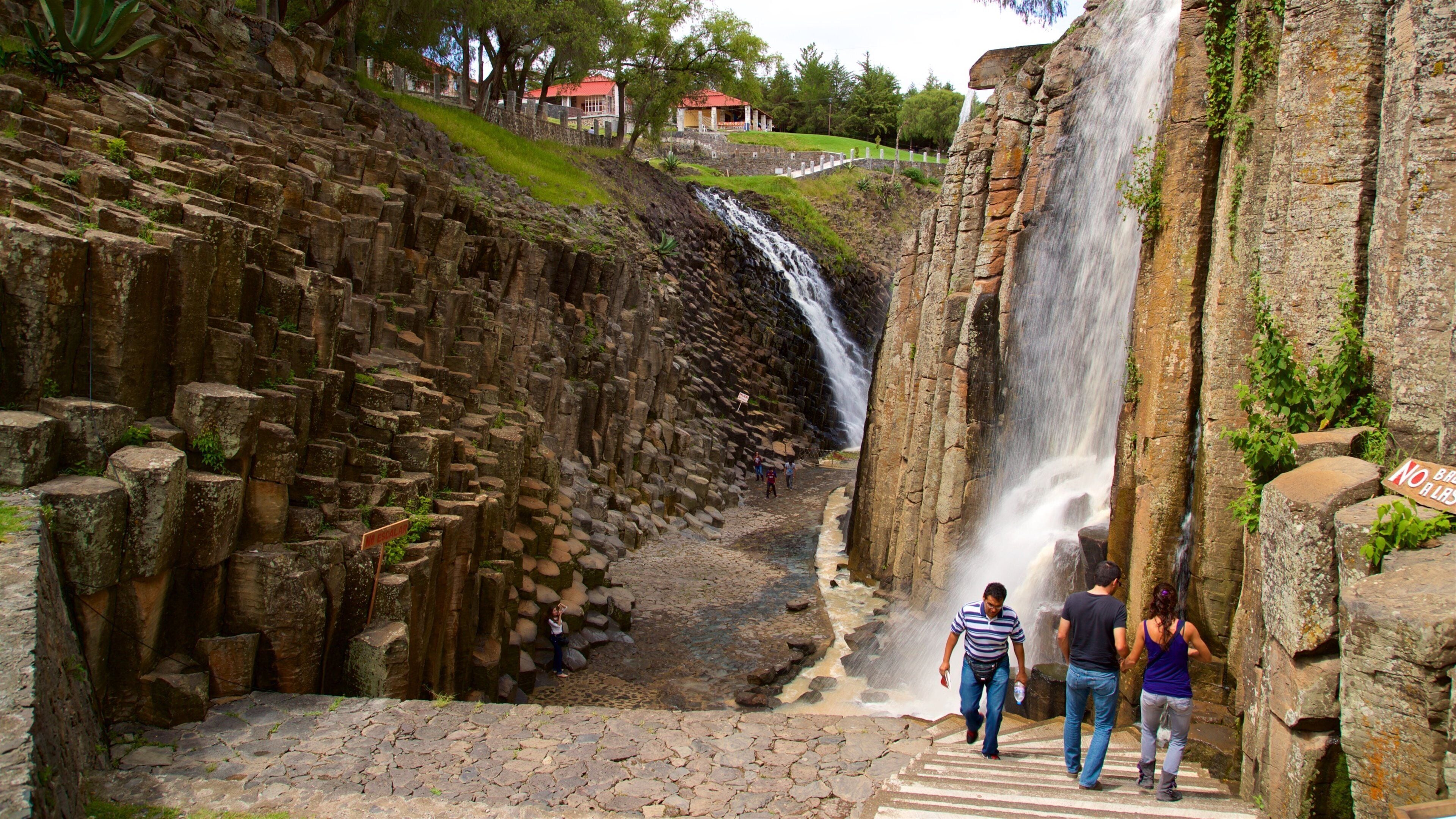 A waterfall cascading down a rocky cliff, with a stone pathway leading to a viewing area.