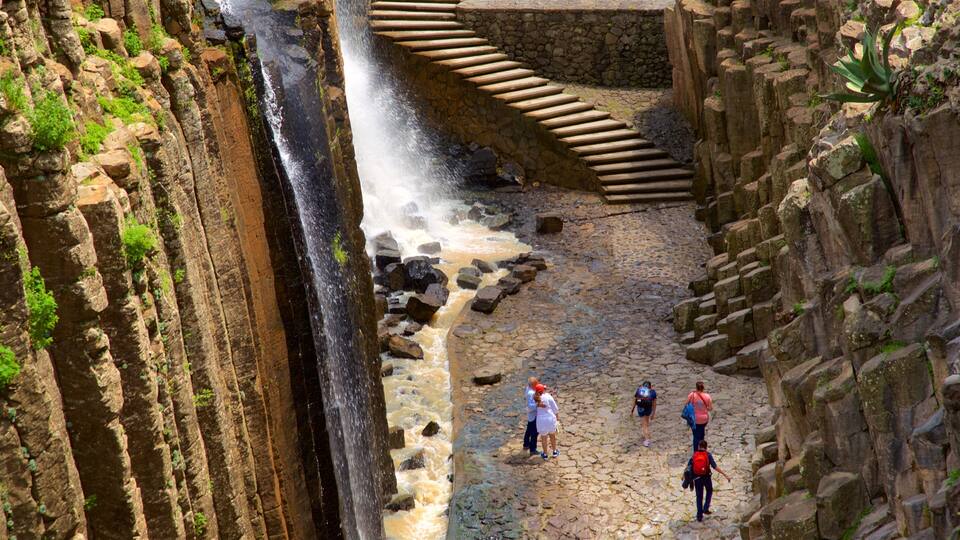 A waterfall cascading down a rocky gorge with a stone staircase leading up.