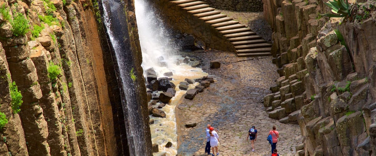 A waterfall cascading down a rocky gorge with a stone staircase leading up.