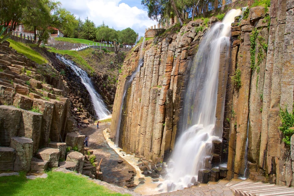 Una cascada se precipita por un risco rocoso, con un sendero de piedra que lleva a un mirador.