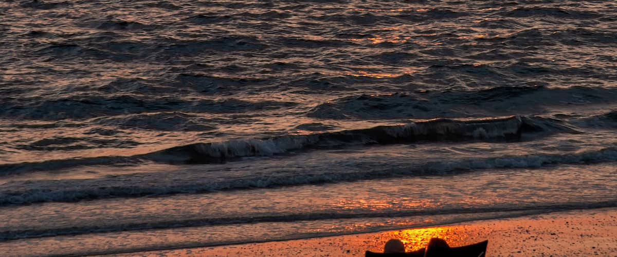 A silhouetted couple in chairs watch the sunset along Bonita Beach in Bonita Springs, Florida.