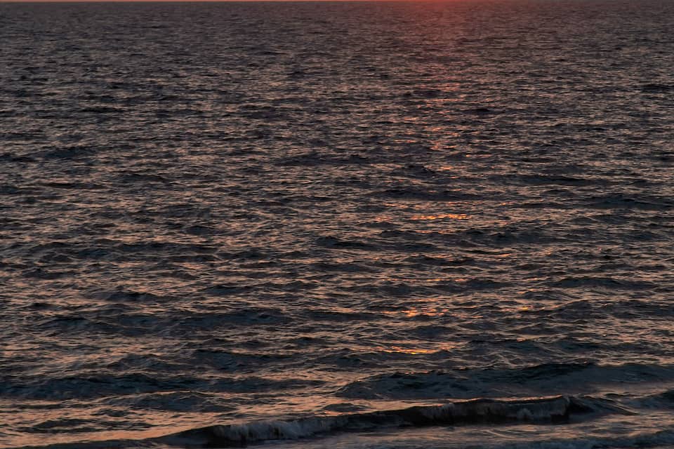 Un sol ponent sobre l'oceà amb una persona relaxant-se en gandules de platja.