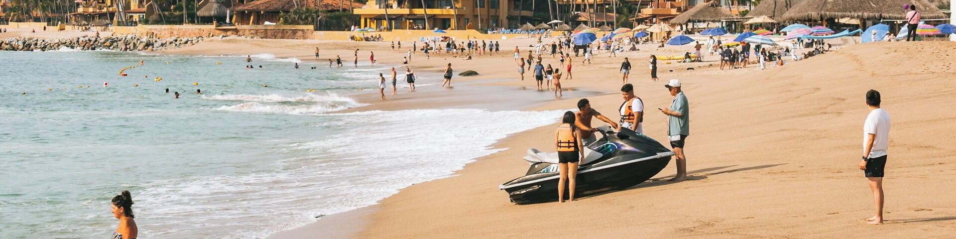 A beach with people, a jet ski, and palm trees.
