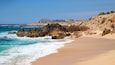 A sandy beach with rocky outcrops and a clear blue ocean.