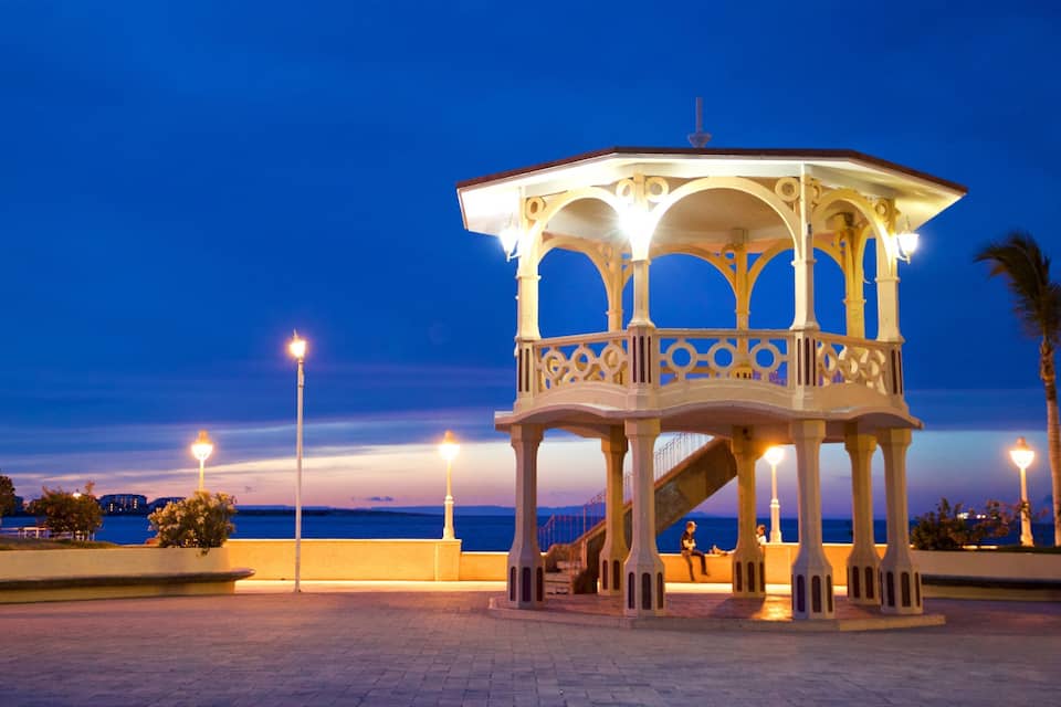 A gazebo with ornate railings and a staircase, overlooking a body of water at dusk.