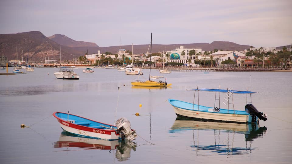 A calm harbor with several boats, including a red and white boat named LAPAZ, B.C.S., and a blue boat with a canopy. In the background, there are buildings and mountains.