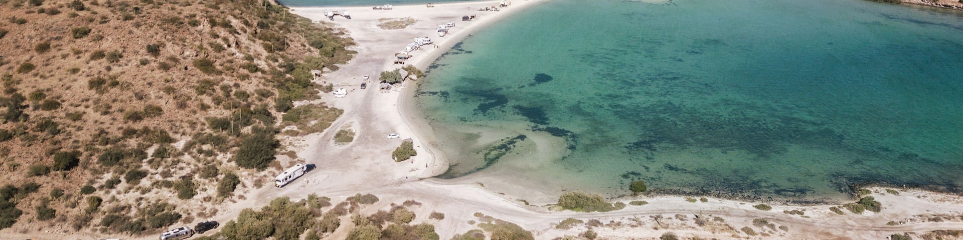 Paisaje costero con aguas turquesas cristalinas, playas arenosas y vegetación escasa.